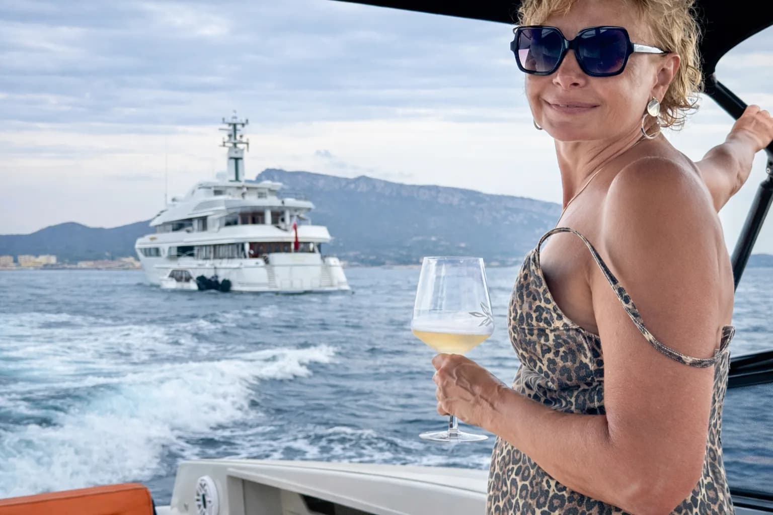 Donna che si gode un calice di vino sulla barca con un superyacht sullo sfondo