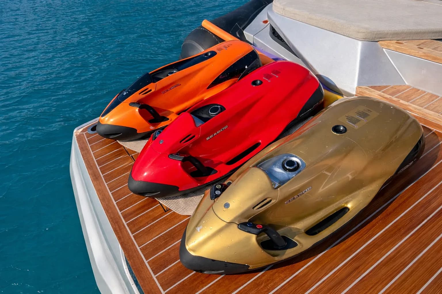 Drei Seabob-Unterwasserscooter in Orange, Rot und Gold auf dem Teakdeck aufgereiht