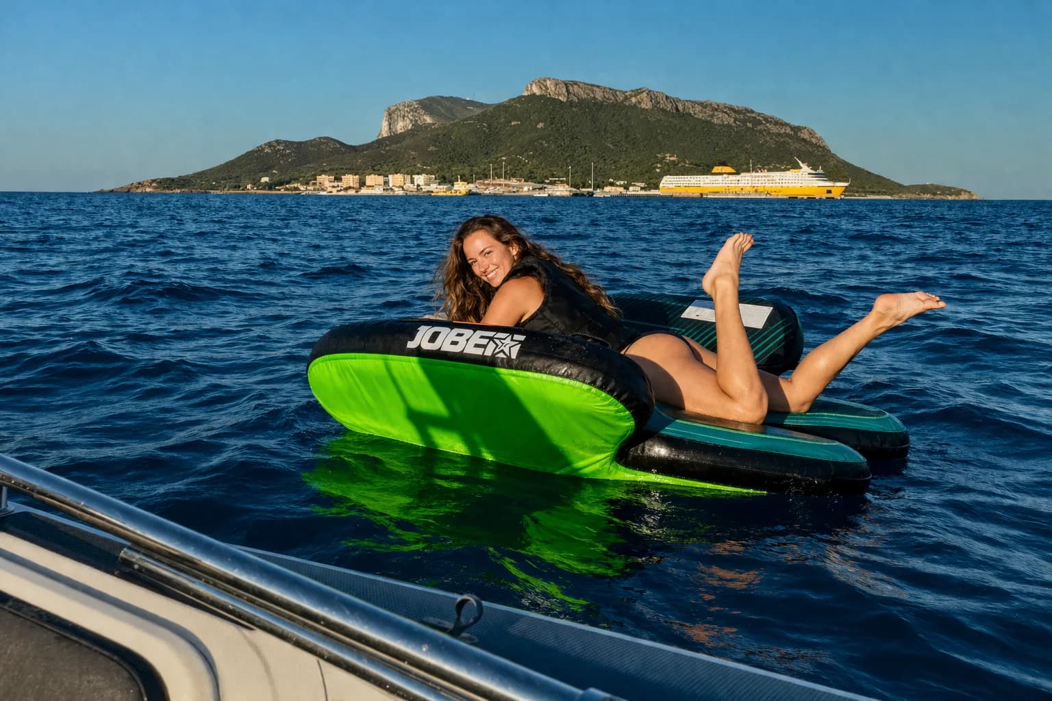 Frau auf Towreifen wird hinter einem Boot gezogen mit sardischer Insel im Hintergrund